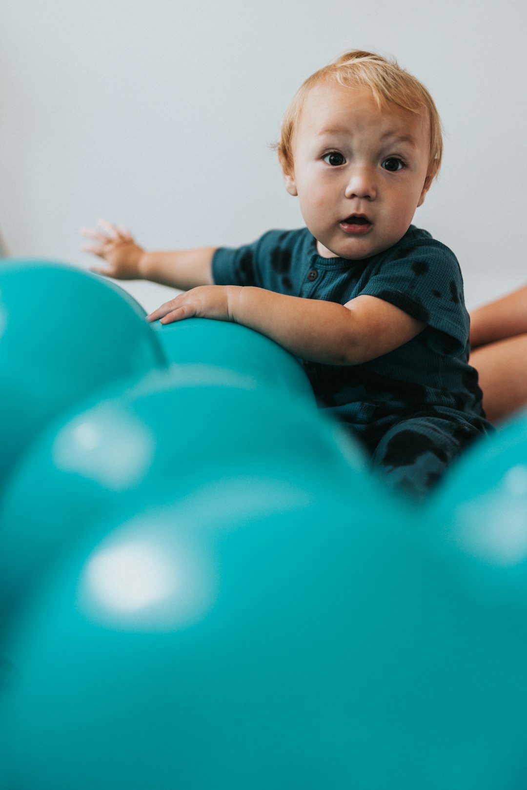 boy-in-blue-and-black-stripe-polo-shirt-lying-on-blue-inflatable-balloons-sjd87ttztk