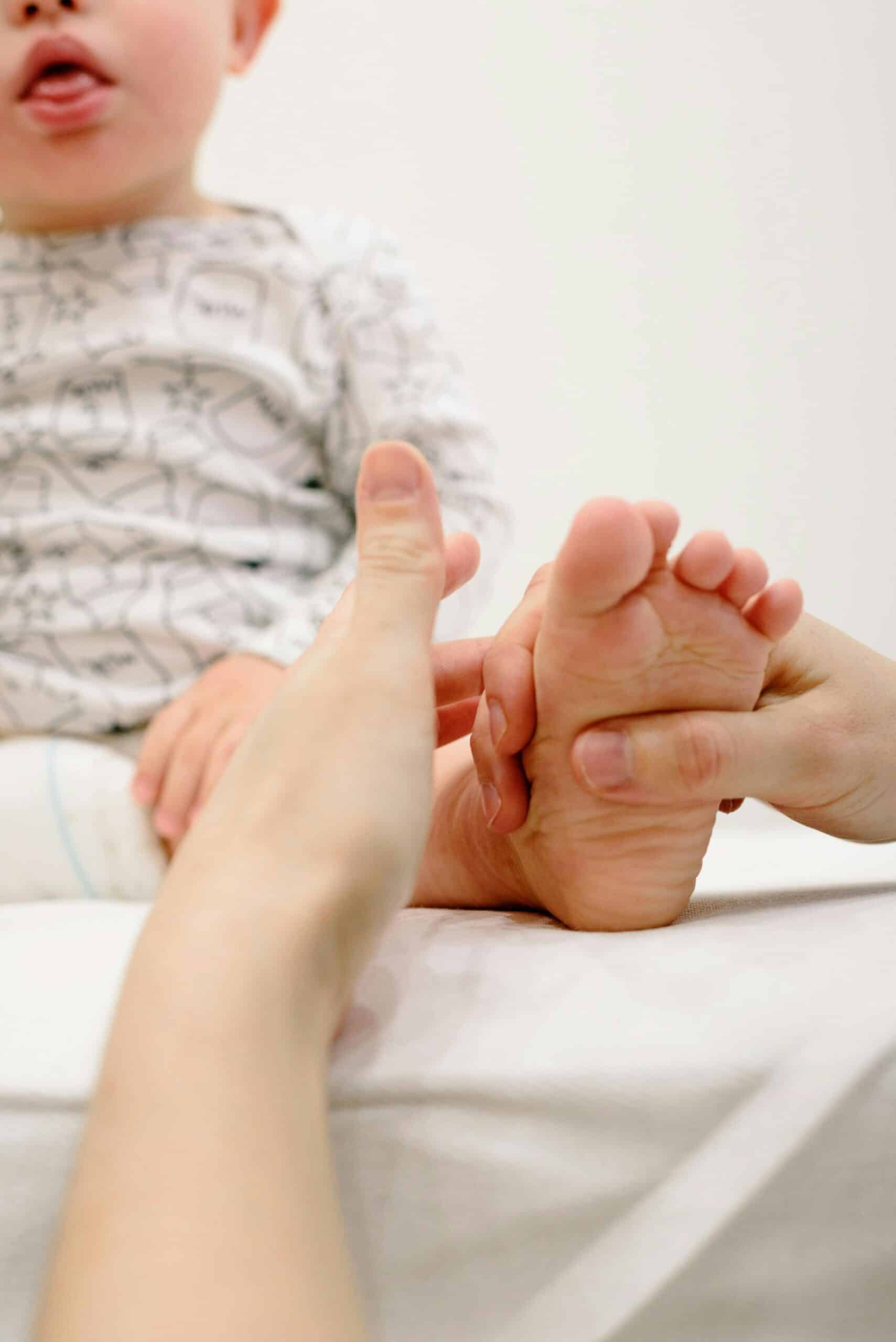 A baby receives a soothing foot massage from an adult in a calm indoor setting.